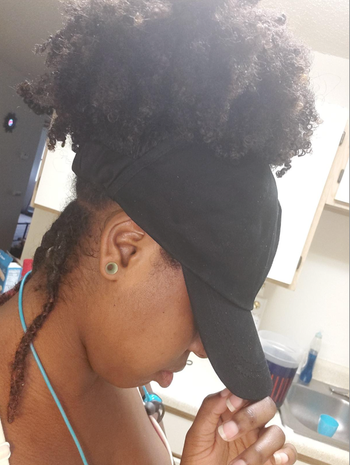 Reviewer sporting the black version of the cap with a curly ponytail peeking through the back opening