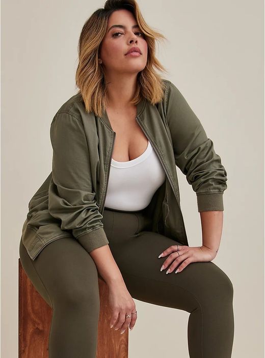 A model sitting, sporting a hunter green twill bomber jacket.