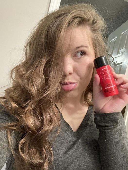 A reviewer with curly, voluminous hair holding the bottle of Big Sexy Hair powder.