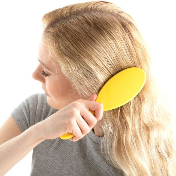 A person brushing long hair with a yellow Drybar brush, demonstrating the use of hair care and styling products