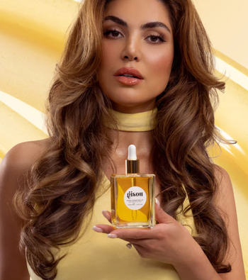 A model showcasing the bottle of Gisou hair oil.