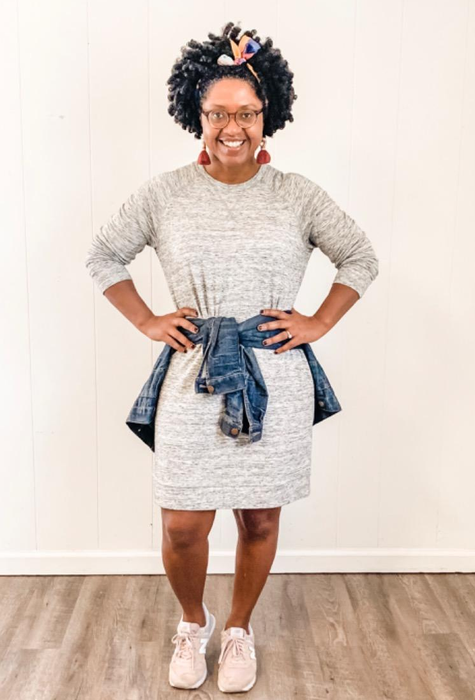The reviewer is seen wearing a light gray dress paired with pink sneakers and a denim jacket tied around the waist.