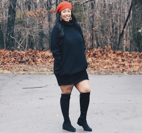 The reviewer is wearing a black dress paired with black boots.