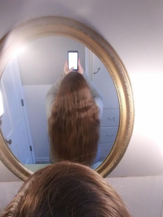 The reviewer with long, wavy, slightly frizzy brown hair, taking a mirror selfie