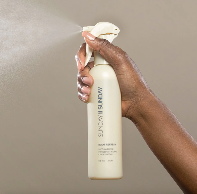 A hand applying the root refresh spray