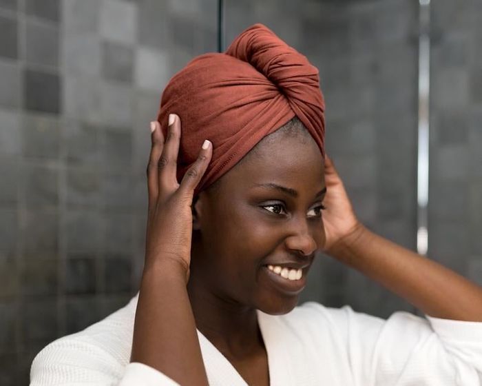 A model with a burnt orange t-shirt towel wrapped around their head