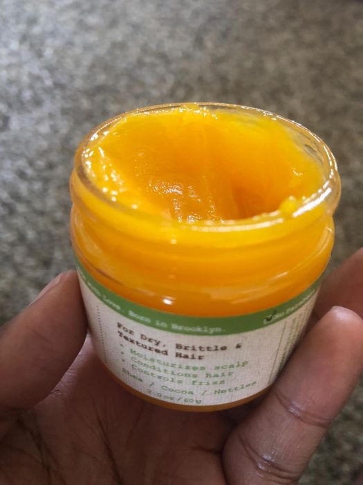 A hand holding the jar of thick, yellow whipped hair treatment