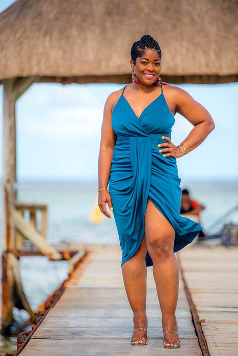 a reviewer wearing the blue version of the dress on a tropical pier by the ocean