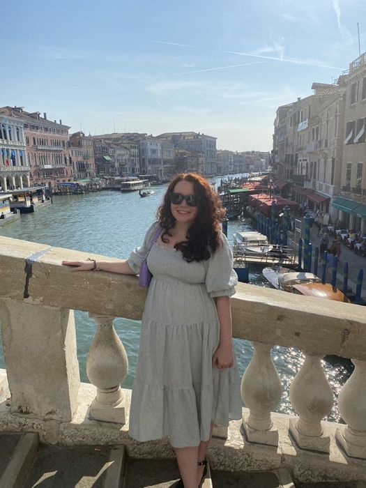 The writer wearing a gingham print midi dress with elbow-length sleeves on a bridge in Venice, Italy.