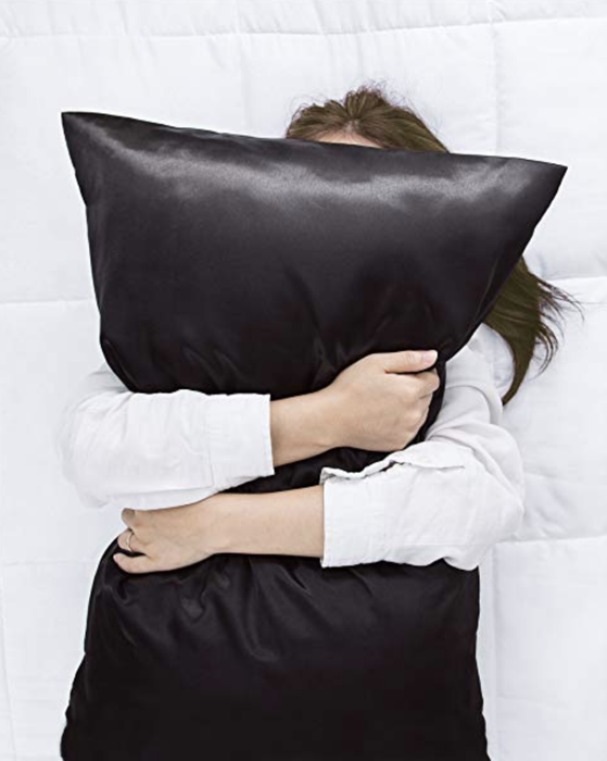 A model cuddling with a pillow featuring a black satin pillowcase
