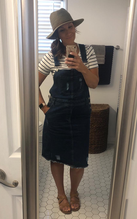 A reviewer in a dark blue denim dress accessorized with a hat