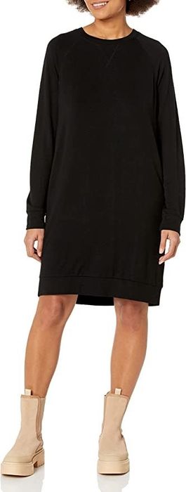 A model is wearing a black dress styled with tan boots.