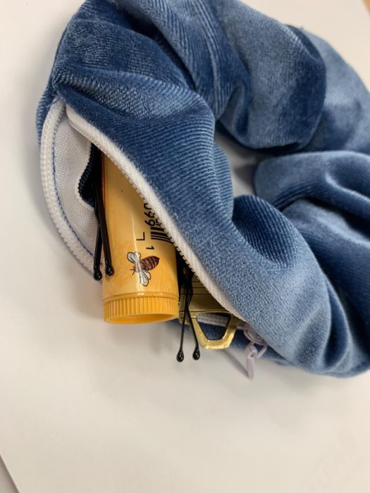 A reviewer's blue velvet scrunchie with a zipper closure, holding lip balm, pins, and other small essentials inside.