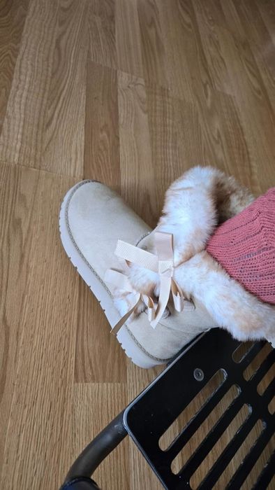 A pair of cozy boots featuring fur lining and a ribbon detail, worn alongside a textured sock for added warmth and style.