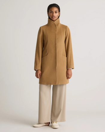 Model in a fitted coat with a high collar, paired with wide-leg pants and loafers, highlighted in a fashion article.