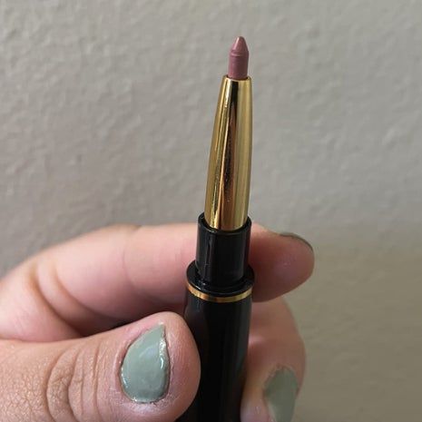A close-up of a hand holding the other side of the dual-ended applicator with a retractable lip liner featuring a sharp, pointed tip, ready to use.