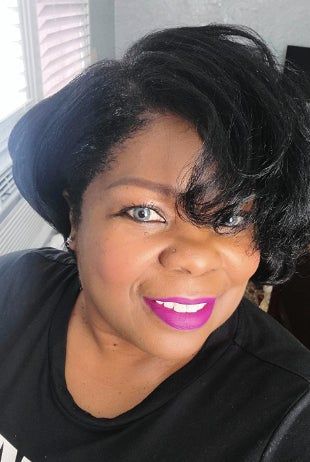 A reviewer beams for a close-up selfie, sporting a black top and vibrant pink lipstick.