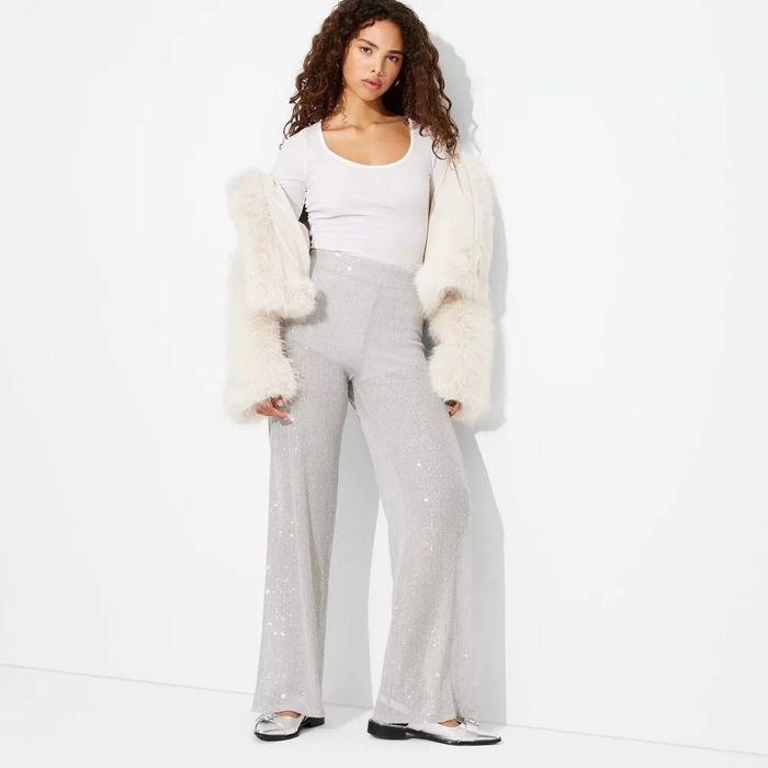 Model wearing a white top, grey sequin pants, and a white fur jacket, showcasing a glamorous look.
