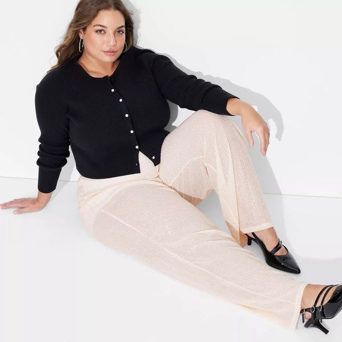 Model sitting casually in a black cardigan and light-colored pants, paired with black shoes, exuding a relaxed vibe.