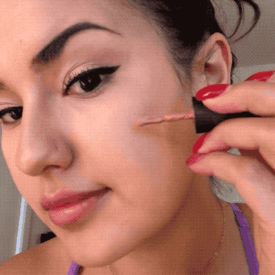 A gif of Kayla applying the blush on her cheeks using a brush applicator.