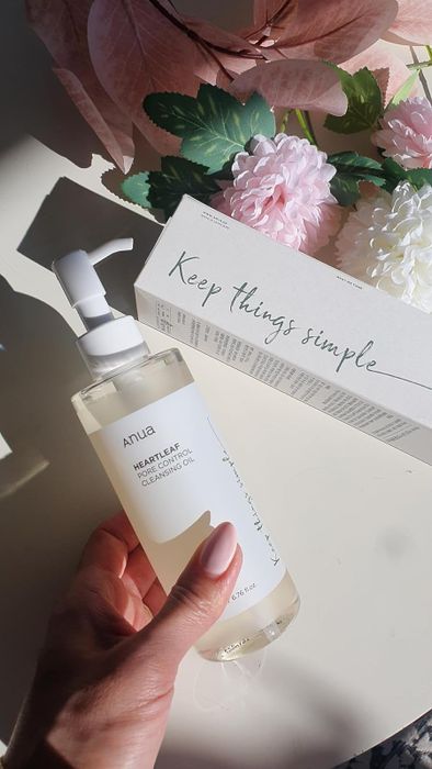 A hand holding the Anua Heartleaf 77% Soothing Cleansing Oil bottle next to its packaging.