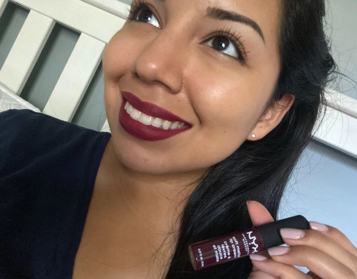 A person smiling while holding a NYX Soft Matte Lip Cream in Copenhagen.