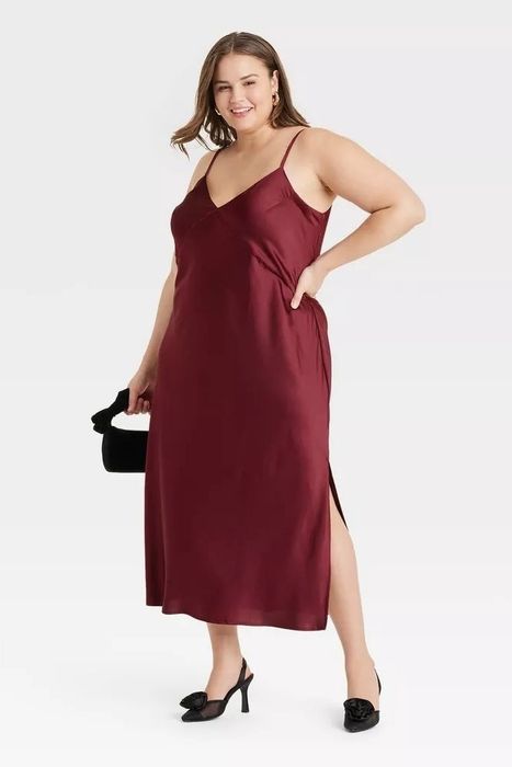 A model wears a sleek, sleeveless dark red dress while holding a handbag, making it an ideal outfit for a chic shopping outing.
