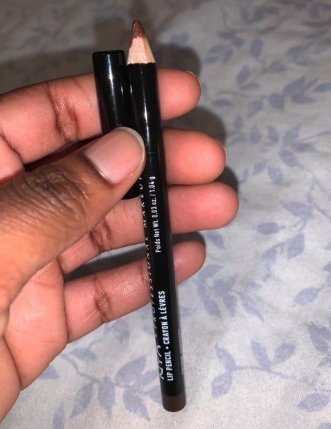 A close-up of a hand holding a brown lip pencil along with its matching cap.