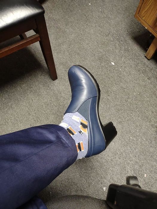 A reviewer wearing blue formal shoes paired with novelty socks that feature coffee mugs, photographed indoors