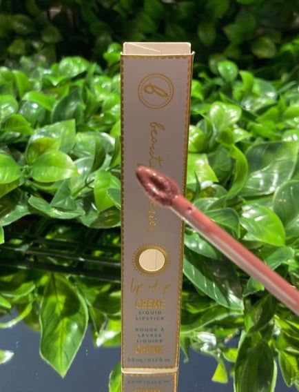 A close-up of the Beauty by Bri liquid lipstick packaging, with the applicator wand showing the product against a leafy backdrop.