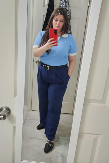 A model taking a mirror selfie, wearing a short-sleeve top and high-waisted navy pants.