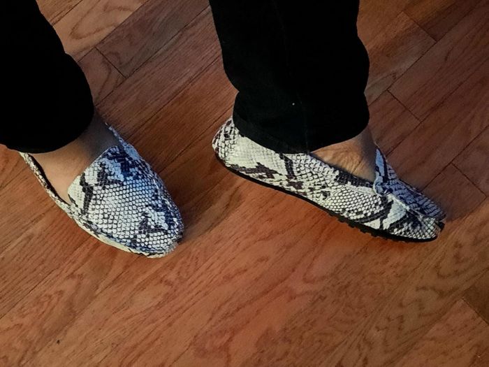 A reviewer flaunting snakeskin-patterned loafers on a wooden floor.