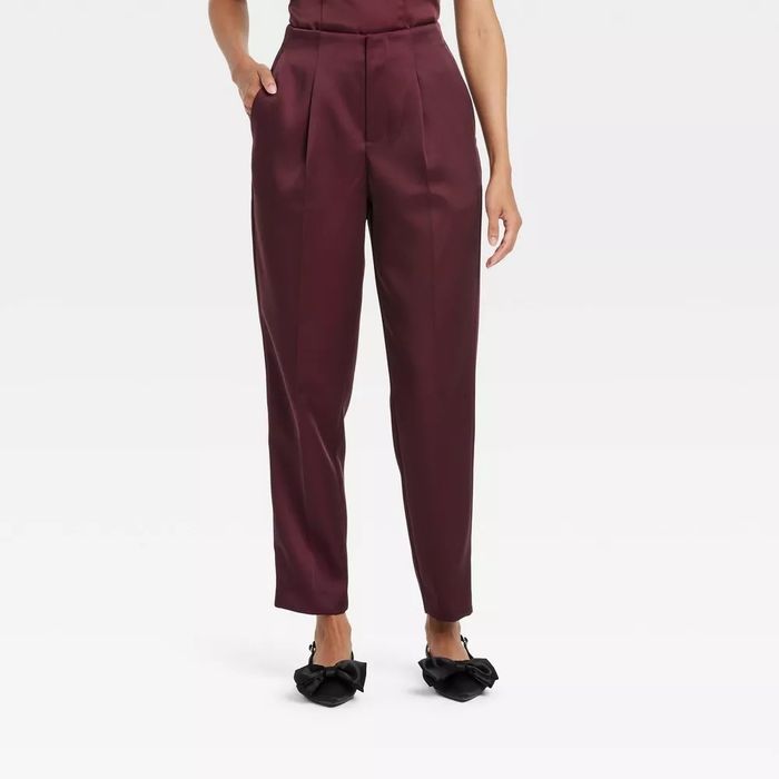 Person wearing chic pleated trousers and black bow-tie shoes, hands in pockets, exuding confidence.