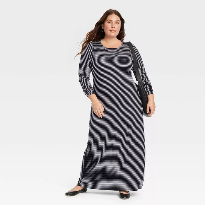 Person wearing a long striped dress, black flats, carrying a black bag, posing for a shopping feature.