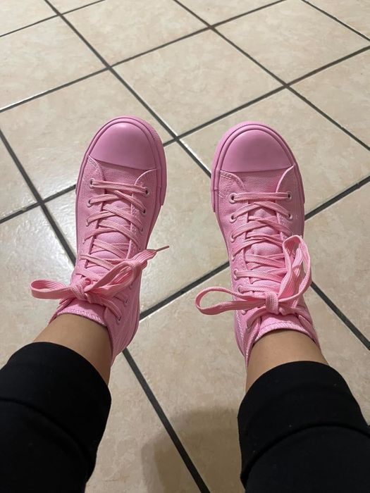 A reviewer rocking pink high-top sneakers, paired with black pants, standing on a tiled floor.
