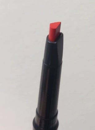 A close-up of a red lip liner in a sleek black tube featuring a distinctive, pointed tip design.