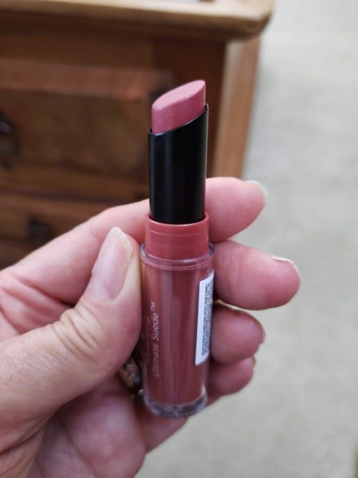 A hand gently holds a pinkish lipstick contained in a transparent tube.