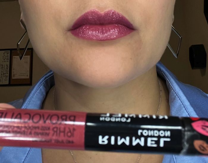 A close-up image of someone wearing pink lipstick while holding the Just Teasing shade of Rimmel London Provocalips 16HR Kiss-Proof Lip Color.