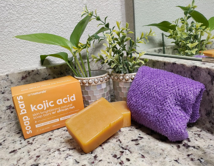 A skincare soap bar and purple washcloth placed on a bathroom countertop next to a plant, with the soap box clearly labeled.