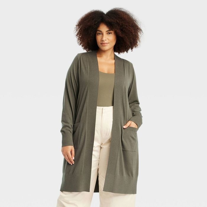 A person poses confidently in a long cardigan, tank top, and wide-leg pants, against a neutral backdrop.