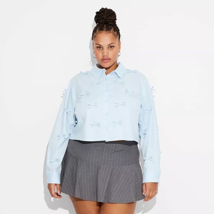Model wearing a light blouse with small bows, paired with a pinstriped skirt, creating a playful yet chic look.