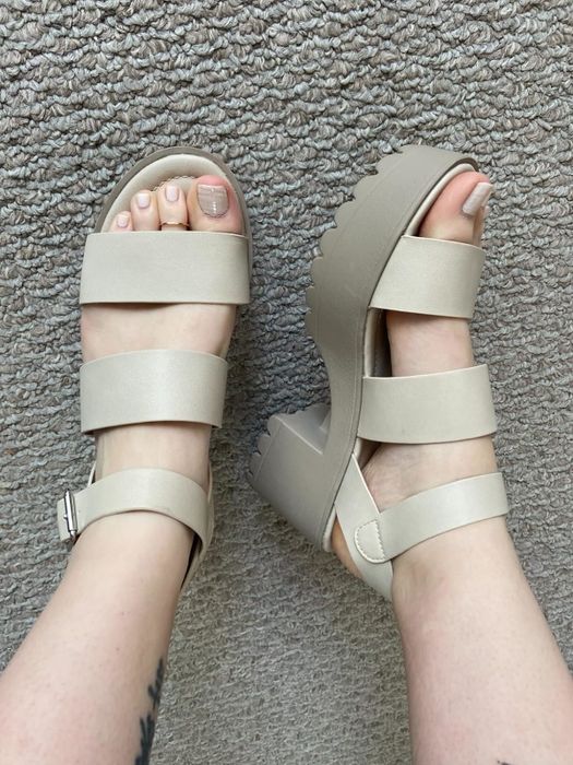 A reviewer wearing beige strappy platform sandals on a carpeted floor, shown from above