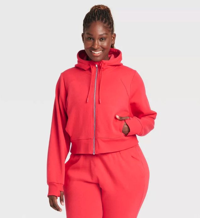 A person models a stylish hooded tracksuit with a zipper, standing and smiling for the camera. Featured in a shopping article.