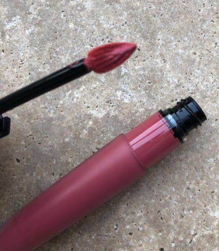 A close-up of a pink liquid lipstick alongside its applicator wand, showcasing its smooth texture.
