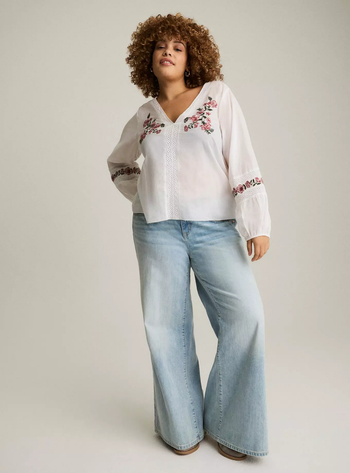 Model sporting an embroidered blouse paired with wide-leg jeans.