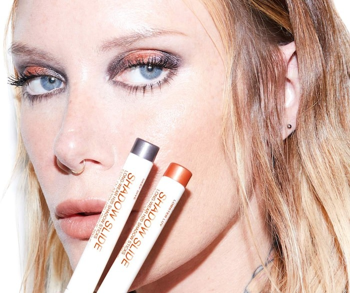 A model holding two eyeshadow sticks, each labeled and worn with the matching colors.