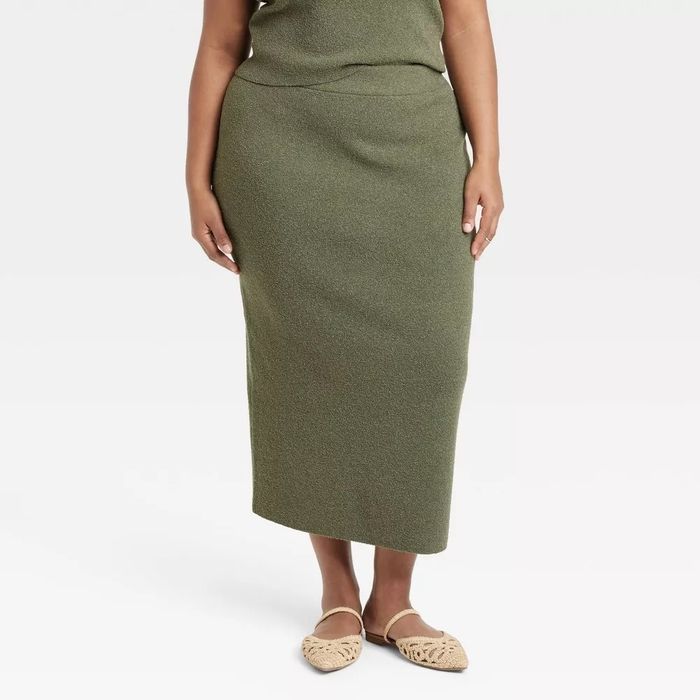 Person wearing a knee-length skirt and woven flat shoes, standing against a plain backdrop.