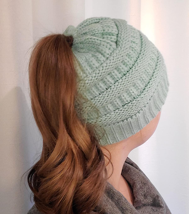 Reviewer showing the back view of a light blue product with a ponytail threaded through it, in front of a white wall