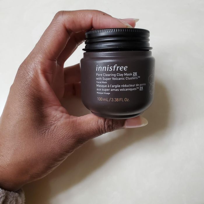 A person's hand holding a jar of Innisfree's Pore Clearing Clay Mask 2X for skincare.