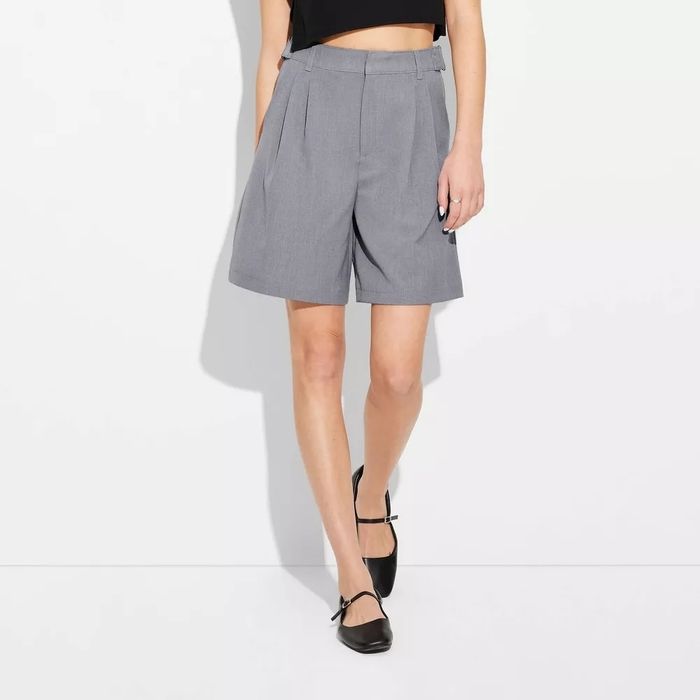 Person dressed in knee-length tailored shorts and strappy flats, exuding a modern, casual style perfect for any laid-back outing.